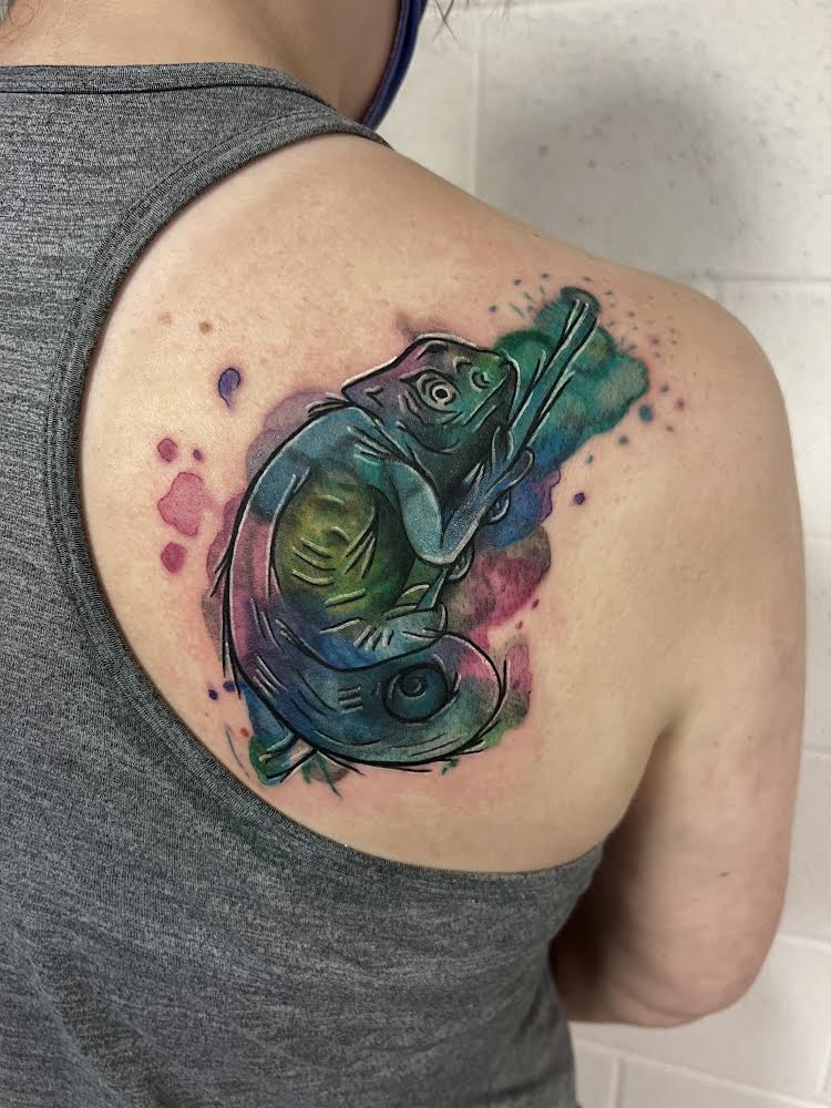 Green, teal, blue, and pink watercolor chameleon tattoo on a woman's shoulder.