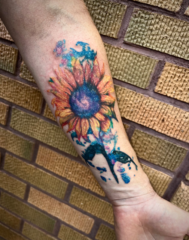 Watercolor galaxy sunflower tattoo on a man's forearm.