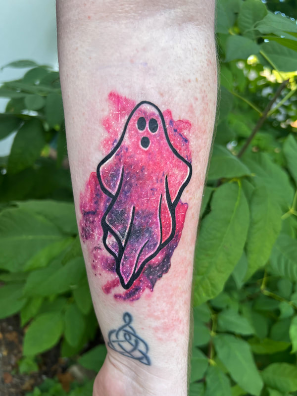 Pink and purple watercolor galaxy ghost tattoo on a woman's forearm.
