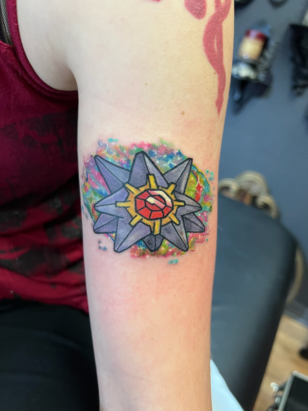 Starmie Pokémon tattoo with rainbow watercolor background on an arm.