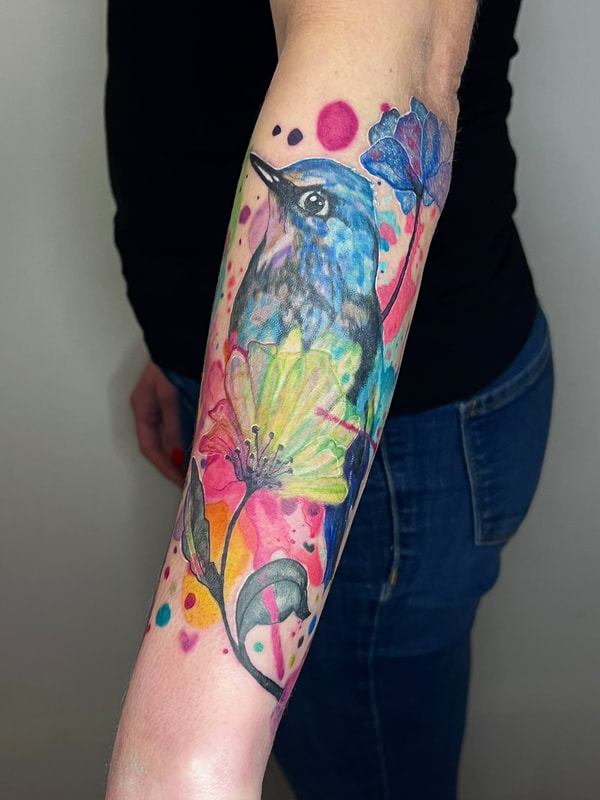 Rainbow watercolor blue bird with neon flowers color realism tattoo on a forearm.