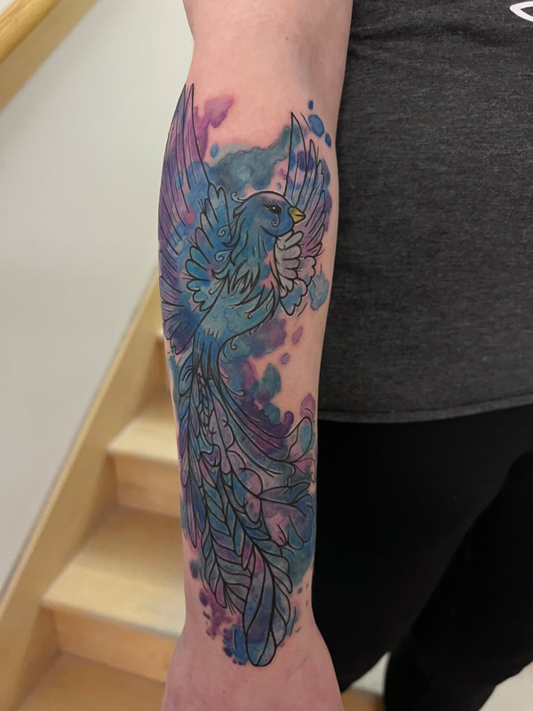 Blue and purple watercolor phoenix tattoo on a woman's forearm.
